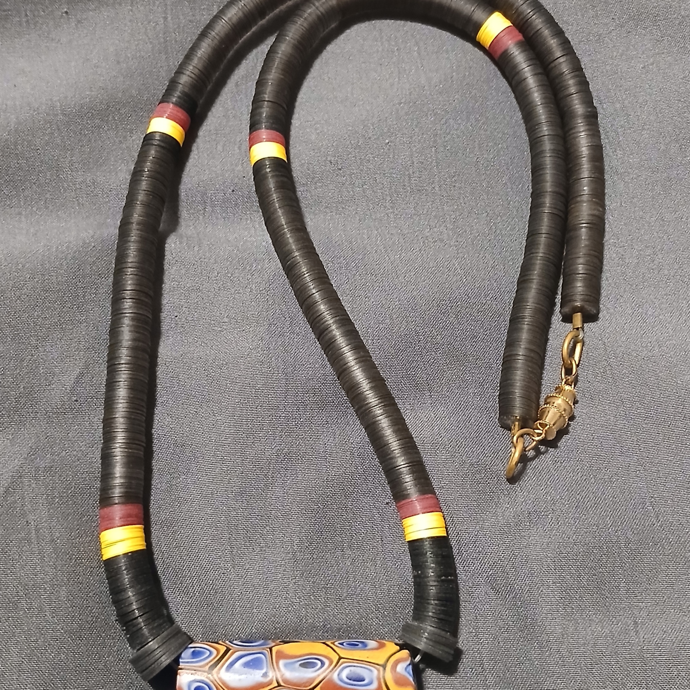 Black Disc Bead Necklace With Yellow And Red Accent Rings And Patterned Pendant